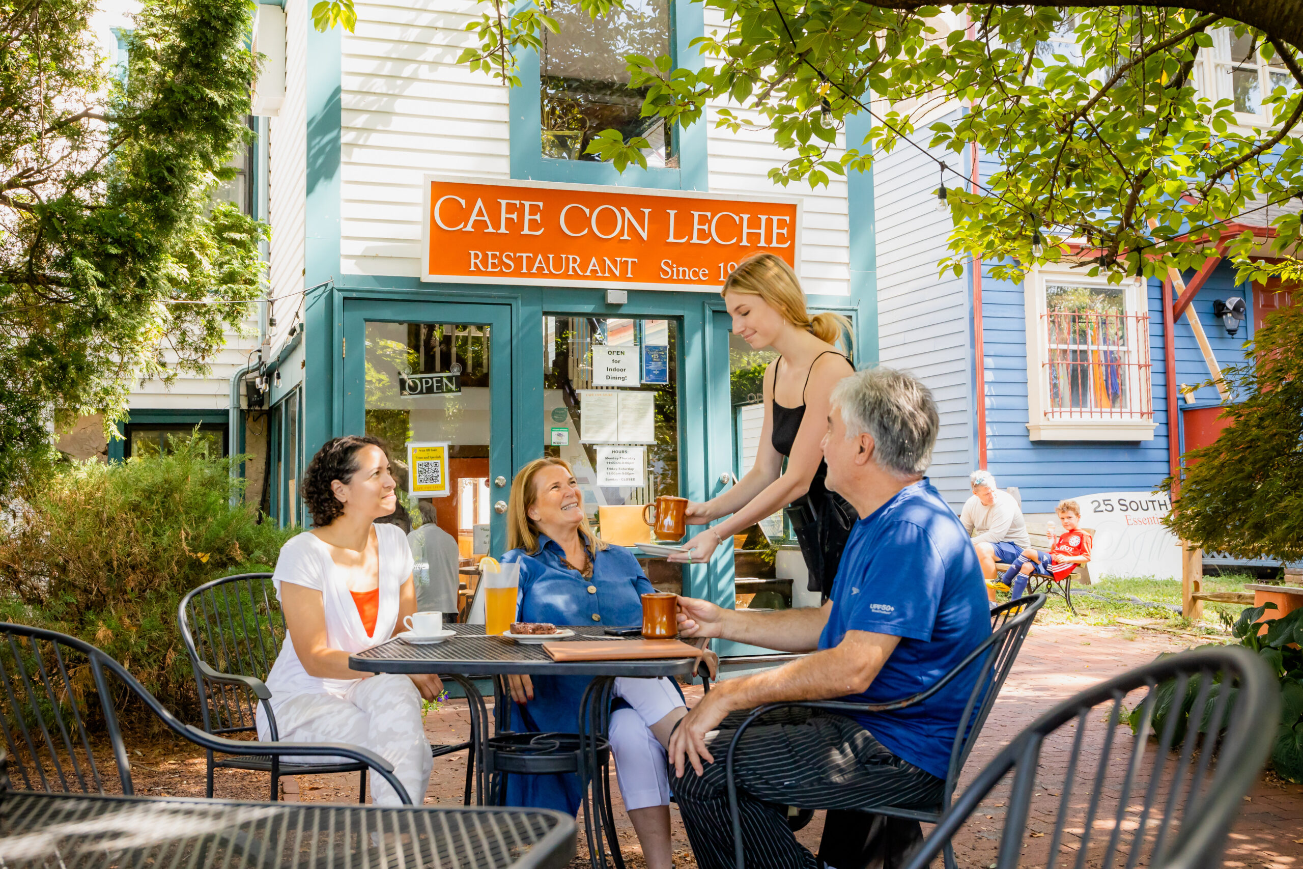 Waitress serving three people coffee at outdoor cafe.
