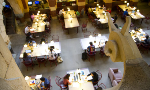 An overhead view of the interior of a library where students sit at tables and study.
