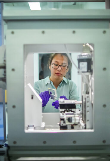 A young woman using protective lab gear examines a piece of nanotechnology lab equipment.