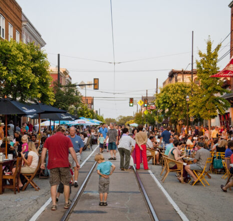 A street full of people enjoying outdoor dining at dusk.